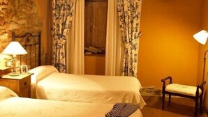Una habitación con dos camas, una mesita de noche con lámpara, una silla y un cuadro en la pared.