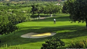 Campo de golf con un green cuidado, un búnker de arena y una persona en el tee.