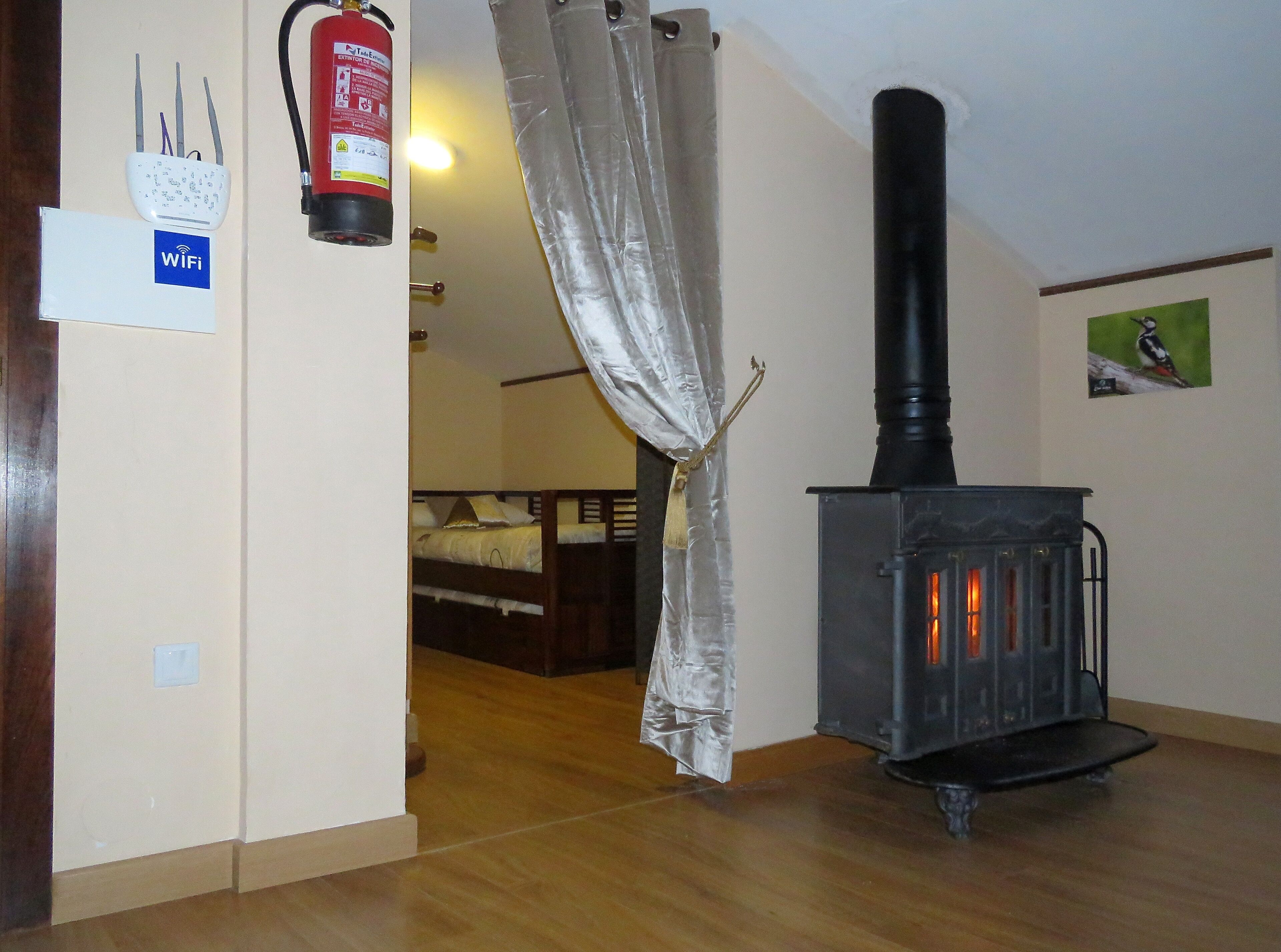 Une pièce avec un poêle à bois, un lit à baldaquin blanc, un panneau indiquant la présence d’une connexion Wi-Fi et un extincteur.
