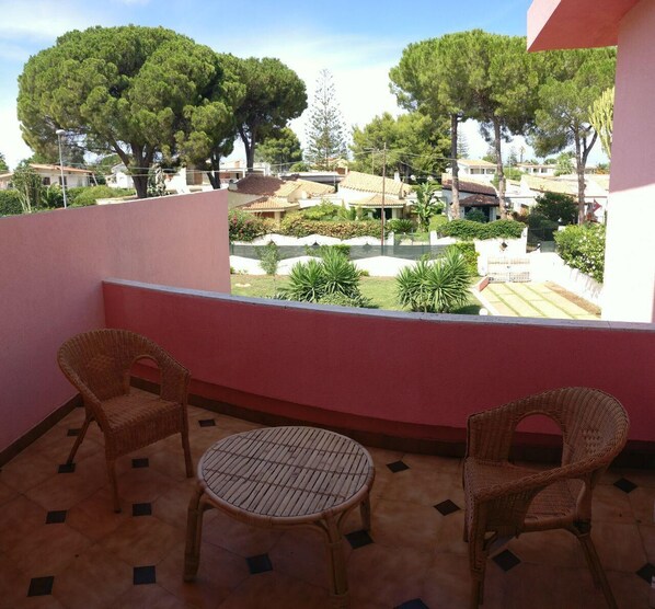 A balcony with two wicker chairs and a small round table, overlooking a residential area with trees and houses. - Villa Rosa - Fontane Bianche - two independent apartments with pool by the sea (Fontane Bianche)