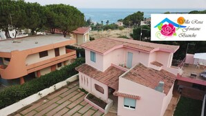 A residential building with a pink facade, terracotta roof tiles, and a paved courtyard with a lawn. - Villa Rosa - Fontane Bianche - two independent apartments with pool by the sea (Fontane Bianche)