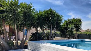 A swimming pool with a wooden deck, surrounded by palm trees and a building in the background. - Villa Rosa - Fontane Bianche - two independent apartments with pool by the sea (Fontane Bianche)