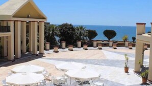 A hotel patio with outdoor seating, palm trees, and a view of the sea. - Comfortable in Elviria (Marbella)