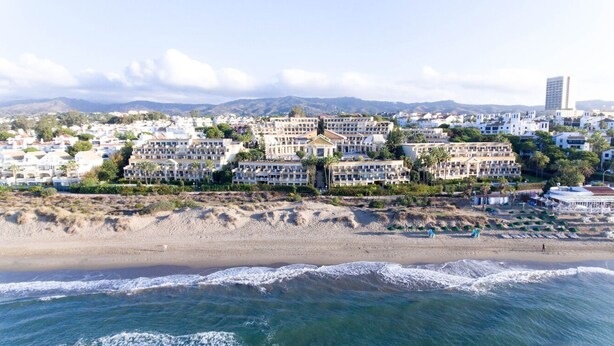 A coastal hotel with multiple buildings, a beach in the foreground, and mountains in the background. - Comfortable in Elviria (Marbella)