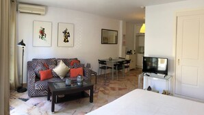 A hotel room with a sofa, a coffee table, a TV, a bed, a dining area, and artwork on the walls. - Comfortable in Elviria (Marbella)