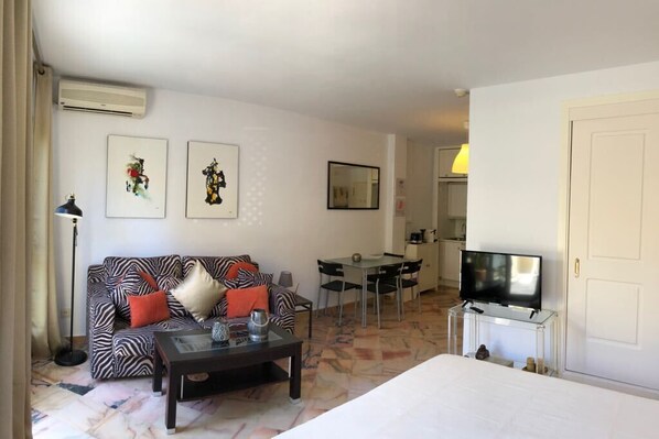 Habitación de hotel con sofá, mesa de centro, televisor, cama, zona de comedor y obras de arte en las paredes.
