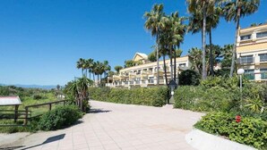 A pathway leading to a multi-story building with balconies, surrounded by palm trees and greenery. - Comfortable in Elviria (Marbella)