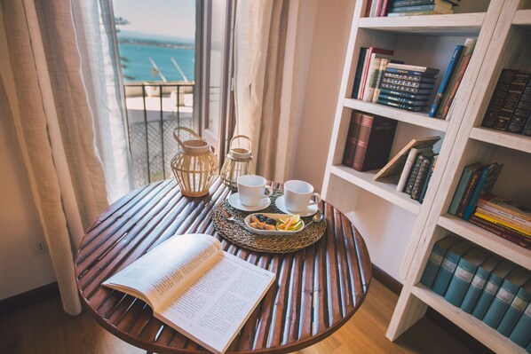 Relax in a serene space with a view of the sea, surrounded by books and a comfortable reading nook.