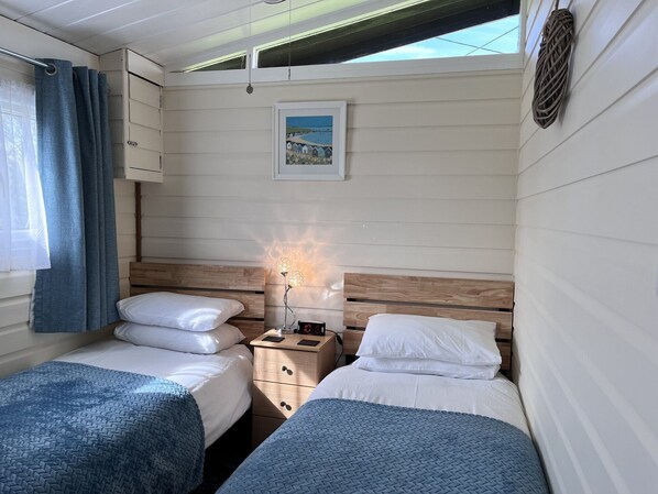 A bedroom with two beds, a nightstand, a lamp, and a framed picture on the wall. - Cedar Lodge, Cedar Springs, Heacham. Only 5 Minutes Walk to the Beach. (Heacham)