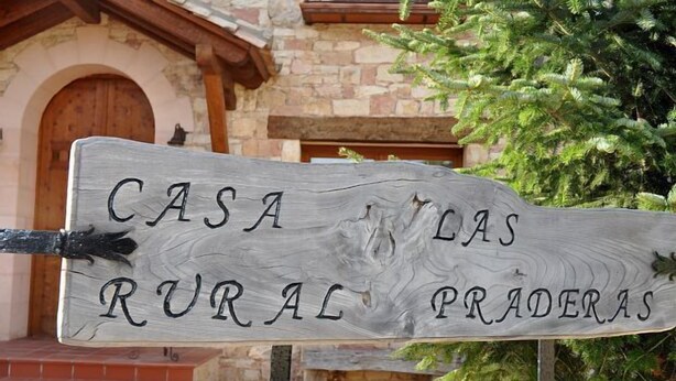 Un letrero de madera rústico con el texto "CASA LAS RURAL PRADERAS" que indica una casa o propiedad rural.