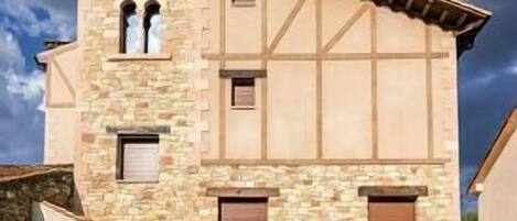 Ein zweistöckiges Steinhaus mit Satteldach, zahlreichen Fenstern und einem kleinen Rasen mit einer Palme.