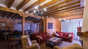 Un interior rústico con vigas de madera a la vista, un sofá rojo y una zona de comedor con muebles de madera.
