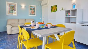 A dining area with a table set for four, yellow chairs, a beige sofa, and a white cabinet with shelves. - Villa Ananda con vista mare, piscina e jacuzzi (Scopello)