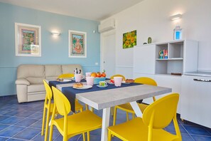A dining area with a table set for four, yellow chairs, a beige sofa, and a white cabinet with shelves.
