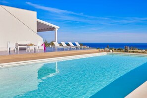 A poolside area with lounge chairs and a covered seating area, overlooking a clear blue sky and ocean. - Villa Ananda con vista mare, piscina e jacuzzi (Scopello)