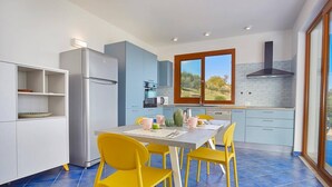 A modern kitchen with a dining table, yellow chairs, and a view of the outdoors through a window. - Villa Ananda con vista mare, piscina e jacuzzi (Scopello)