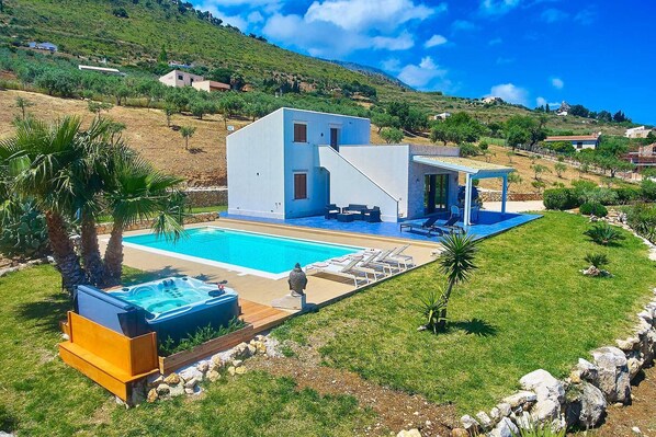 Une maison moderne à deux étages, dotée d’une piscine, d’un espace extérieur aménagé et offrant une vue sur les collines environnantes.