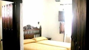 Una habitación con una cama de madera, una mesita de noche y una lámpara fijada a la pared.