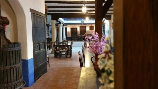Un pasillo con un banco de madera y un jarrón de flores, que conduce a un comedor con mesas y sillas.