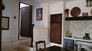 Un comedor con una mesa de madera, sillas, una escalera que sube a un nivel superior y una zona de cocina con salpicadero de azulejos.