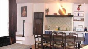 Un comedor con una mesa y sillas de madera, una cocina al fondo y un cuadro en la pared.