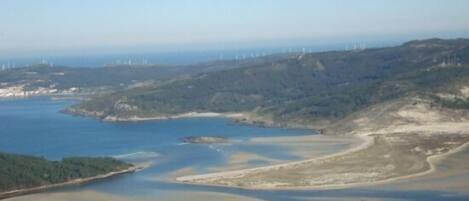 Un paisaje costero con un río, casas y aerogeneradores en la distancia.
