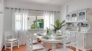 A dining area with a white table set for four, surrounded by white chairs with cushioned seats.