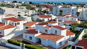 A residential area with white buildings and red-tiled roofs, arranged in a grid pattern with visible driveways and green spaces.