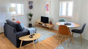 A modern living room with a sofa, a coffee table, a TV, and a dining area with chairs. - Riverview Bright Studio @Graça. New Deco 2023! (Lisboa)