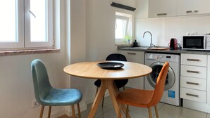A compact kitchen with a round wooden table, two chairs, a washing machine, and a microwave. - Riverview Bright Studio @Graça. New Deco 2023! (Lisboa)