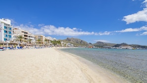 A beach with clear water, sun loungers, umbrellas, and buildings in the background.