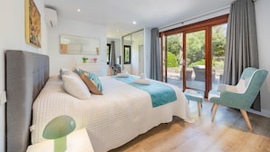 A bedroom with a large bed, a chair, a desk, and a view of the outdoors.