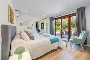 A bedroom with a large bed, a chair, a desk, and a view of the outdoors.