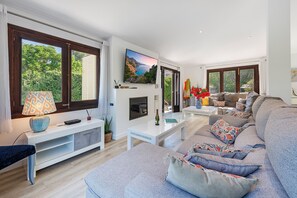 A modern living room with a fireplace, large windows, a sofa, and a TV. - Villa Falco Perfect location by JS Villas (Port de Pollença)