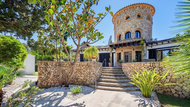 A stone building with a tower, steps leading to the entrance, and a garden with various plants.