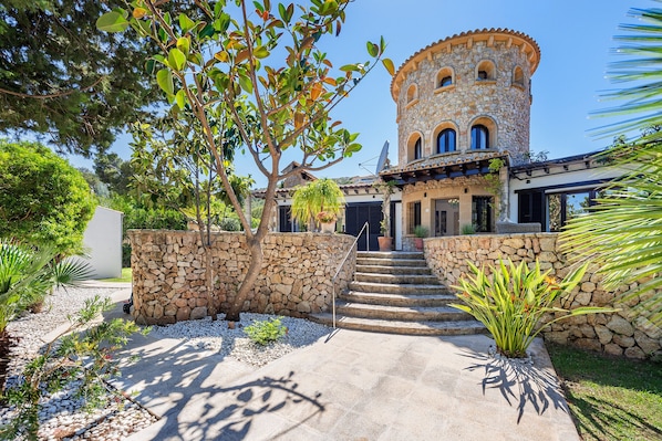 A stone building with a tower, steps leading to the entrance, and a garden with various plants.