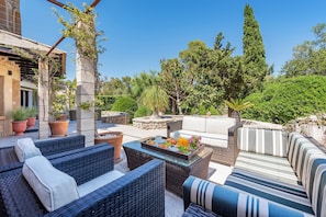 A patio area with wicker furniture, a glass-top table with food, and potted plants. - Villa Falco Perfect location by JS Villas (Port de Pollença)