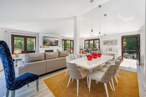 A modern living room with a sofa, dining table, chairs, and a large window.
