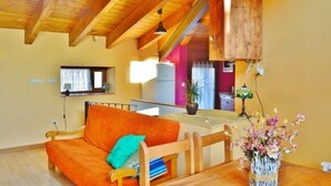 A cozy living room with a wooden ceiling, a sofa, a table with a vase of flowers, and a kitchen in the background. - Casa Javier for 4 people (Rodellar)