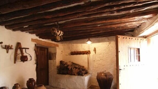 A rustic interior with a wooden ceiling, a wooden door, and a small window. There are several wooden bowls and a large pot on the wall. - Casa Javier for 4 people (Rodellar)