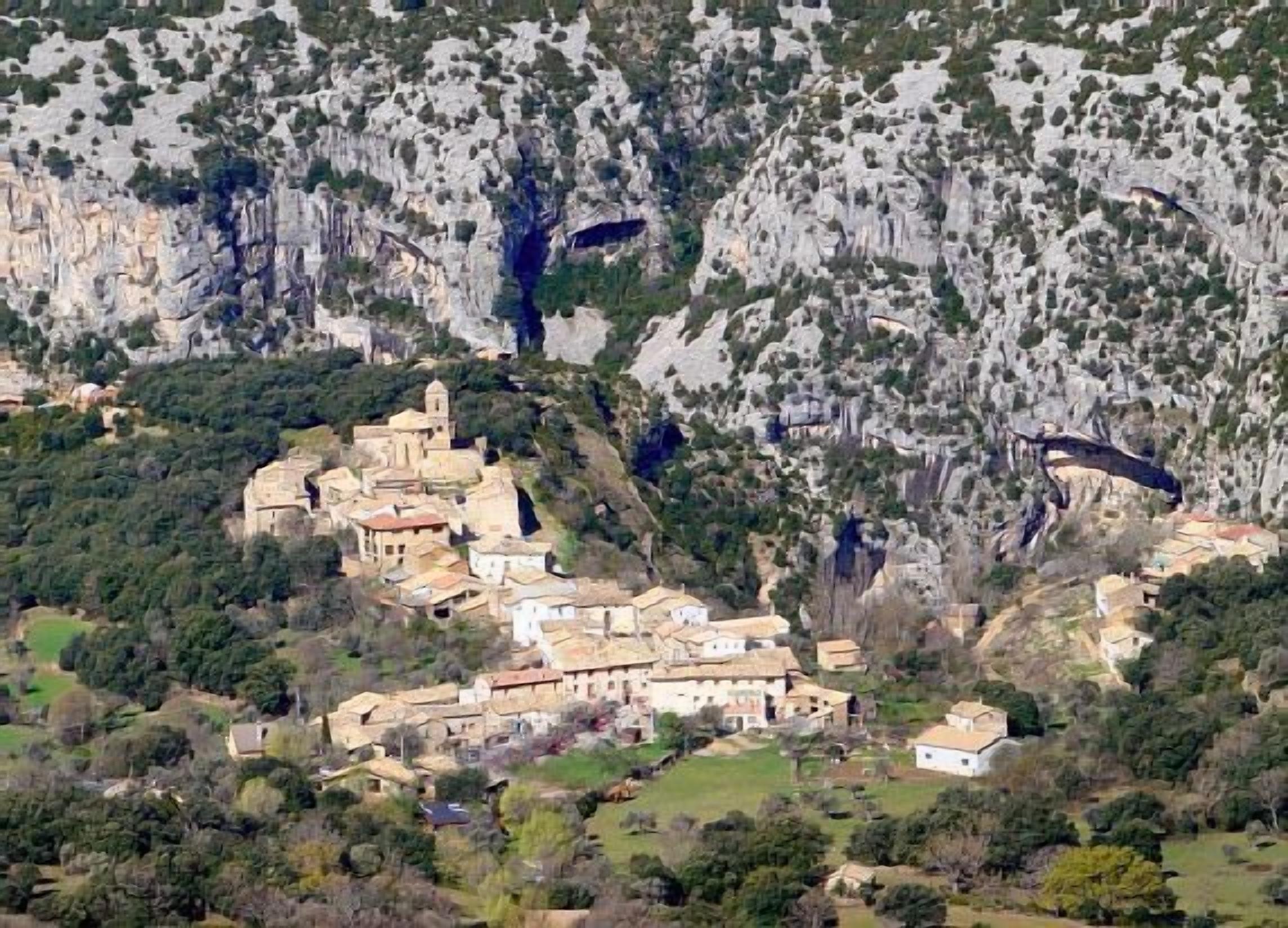 A village nestled in a valley with stone buildings, surrounded by rocky cliffs and greenery.