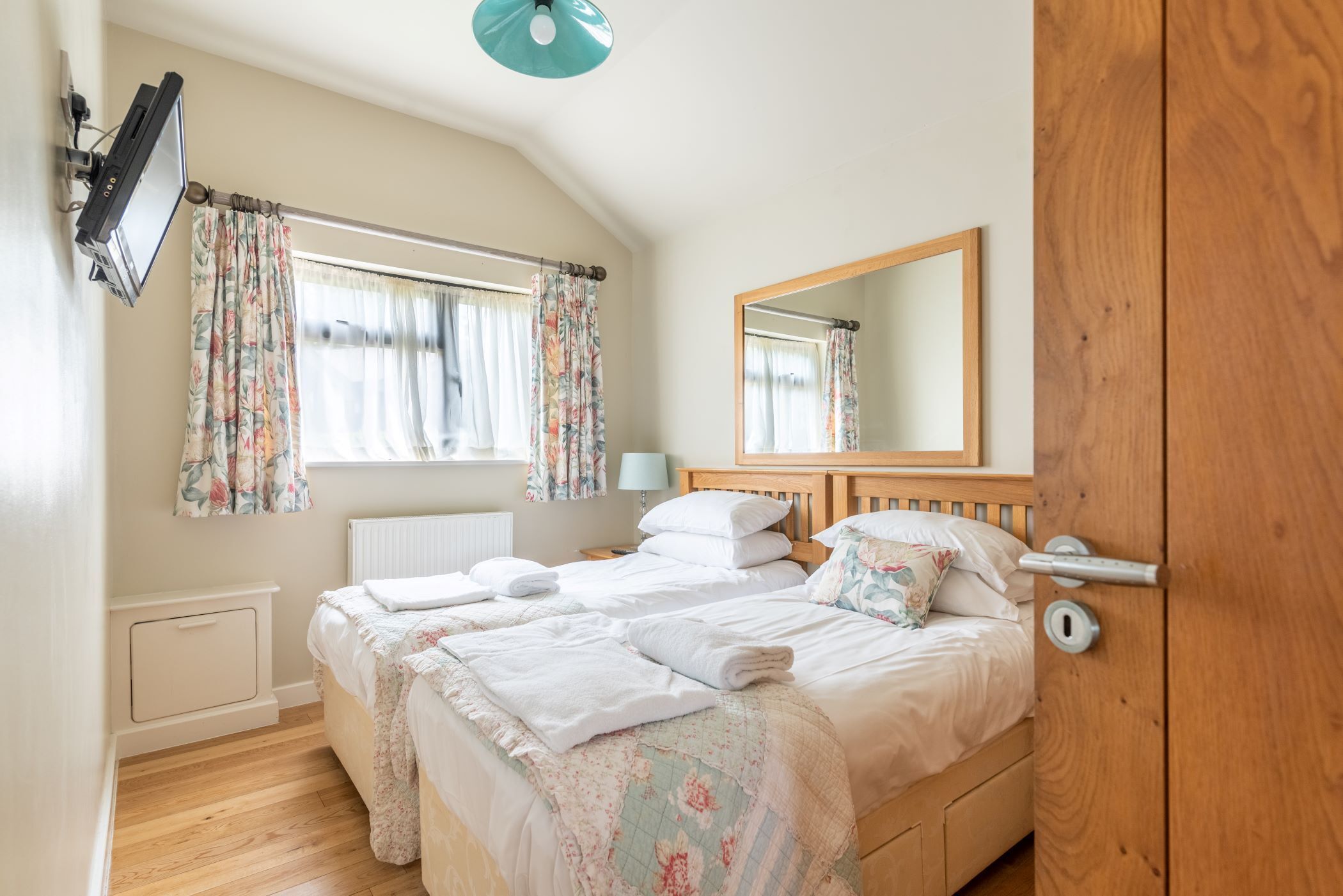 Een slaapkamer met twee bedden, een grote spiegel en een raam met bloemen gordijnen.