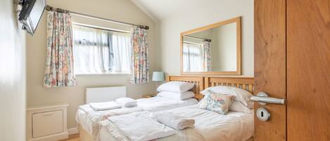 Een slaapkamer met twee bedden, een grote spiegel en een raam met bloemen gordijnen.