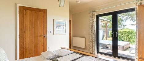 A bedroom with a large bed, a wooden door, a framed picture on the wall, and a view of an outdoor hot tub through a glass door.