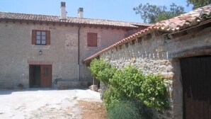 A stone building with a tiled roof, a wooden door, and a small garden area with greenery.