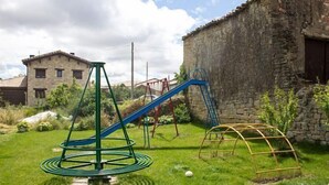 A playground with a swing set and a climbing structure in a grassy area with a stone building in the background.