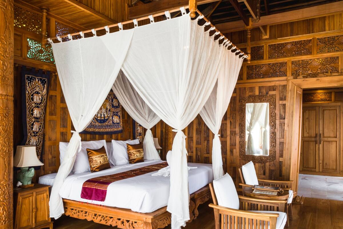 A four-poster canopy bed with white linens, a wooden headboard, and decorative pillows.