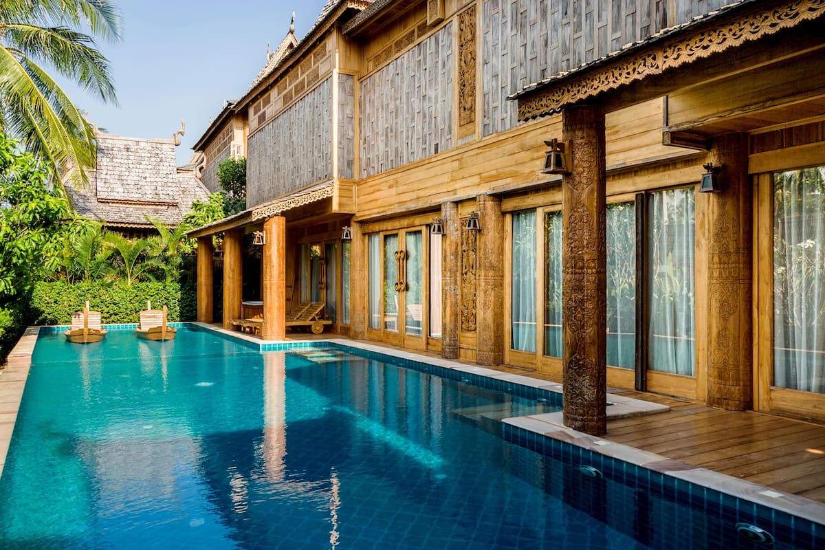 A poolside view of a traditional wooden building with large windows and a clear blue pool.