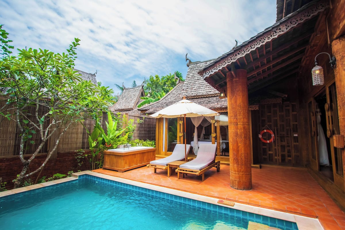 A pool area with two lounge chairs and a canopy, surrounded by wooden structures with traditional architecture.