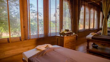 Two single beds with neatly made linens, a wooden nightstand, and a view of the surrounding greenery.